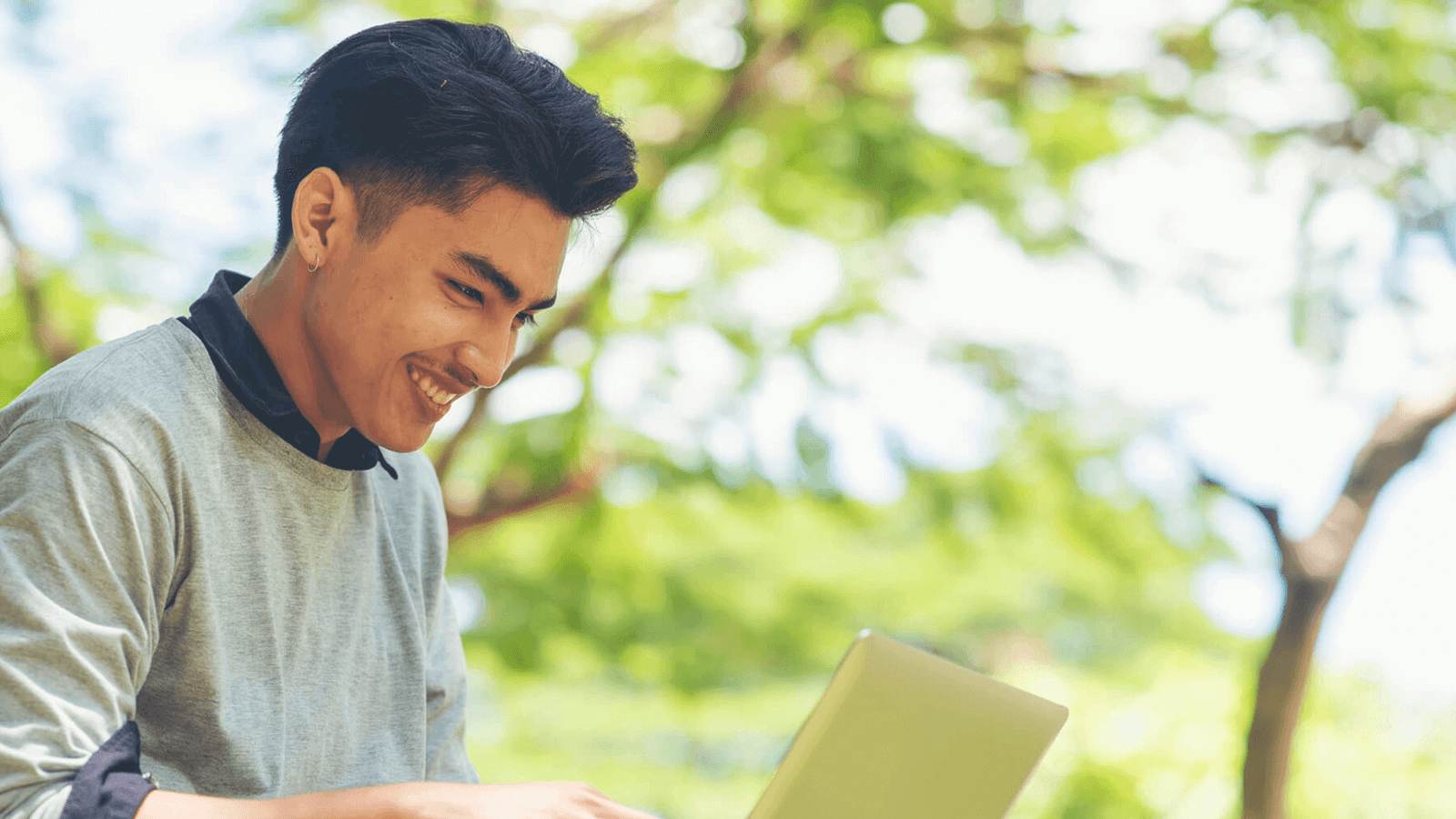 A man seated in a park with a laptop on his lap