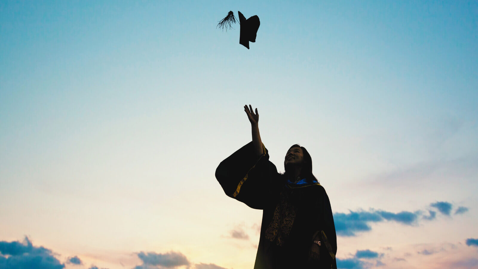 a graduate wearing a gown throws up their cap in the air