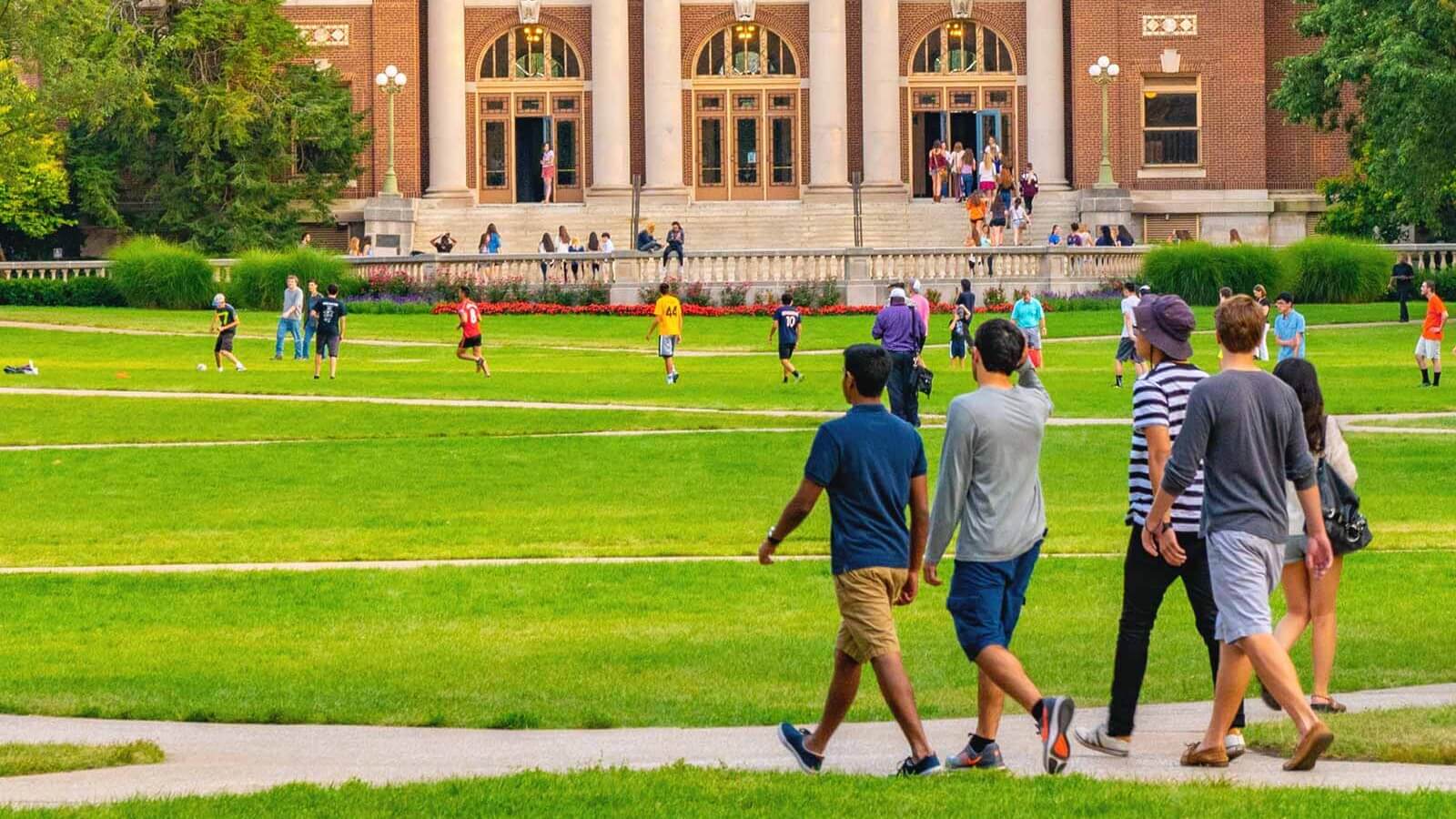 groups of students walking across a college campus quad lawn
