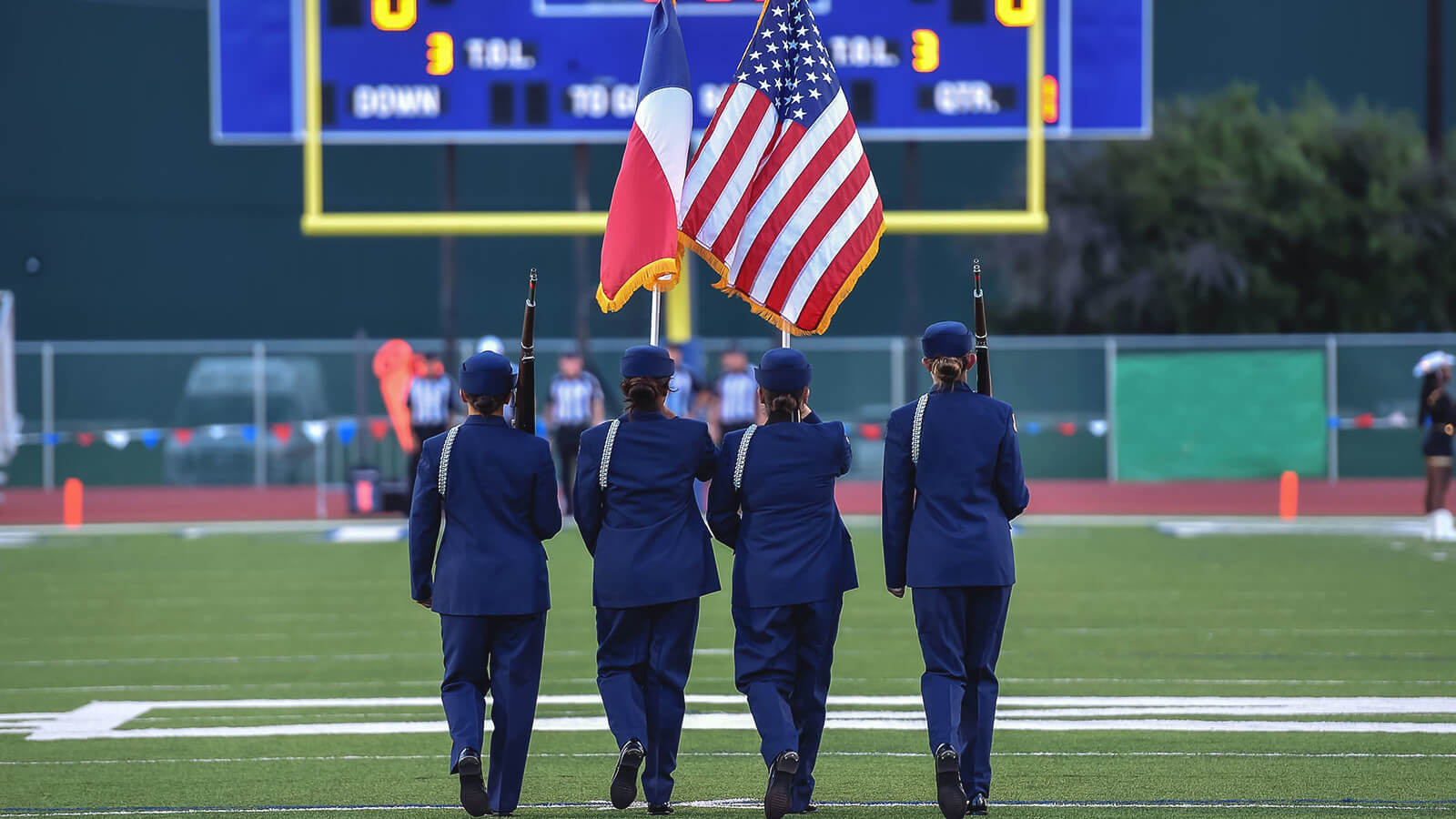 JROTC cadets march with flags on a football field