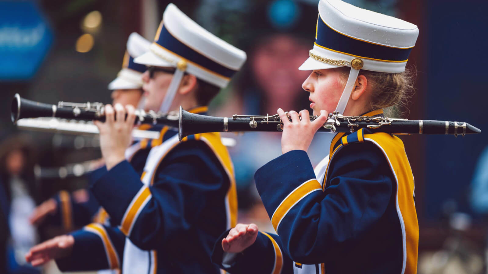 students march in a band wearing blue and gold uniforms and playing instruments