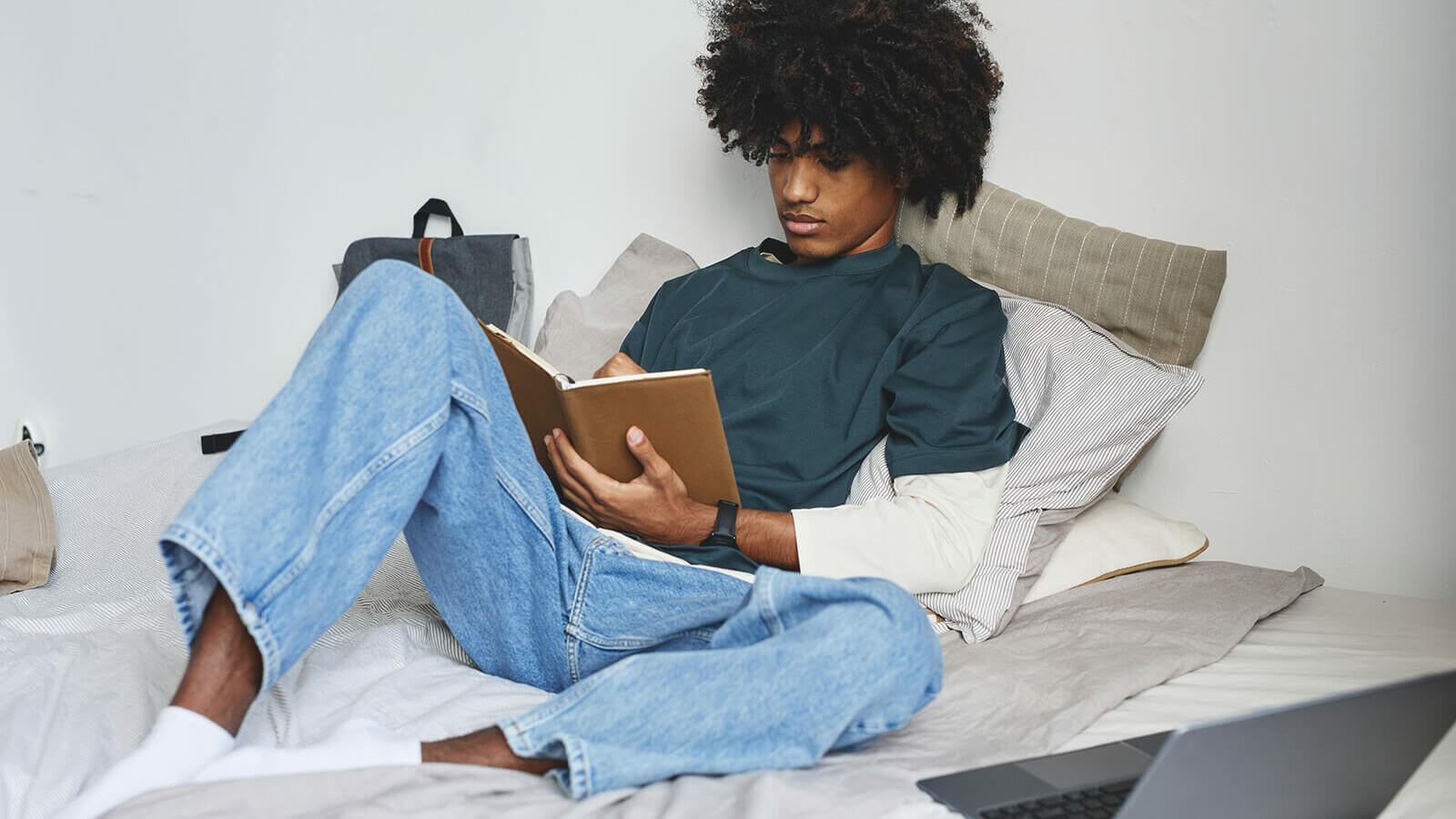 a student studies from a notebook while laying on his bed