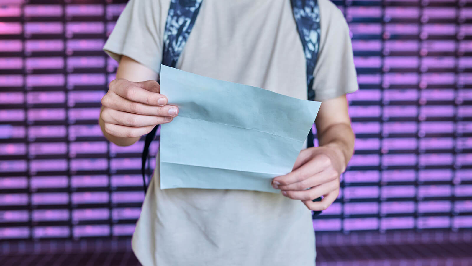 A student wearing a backpack holding a letter.