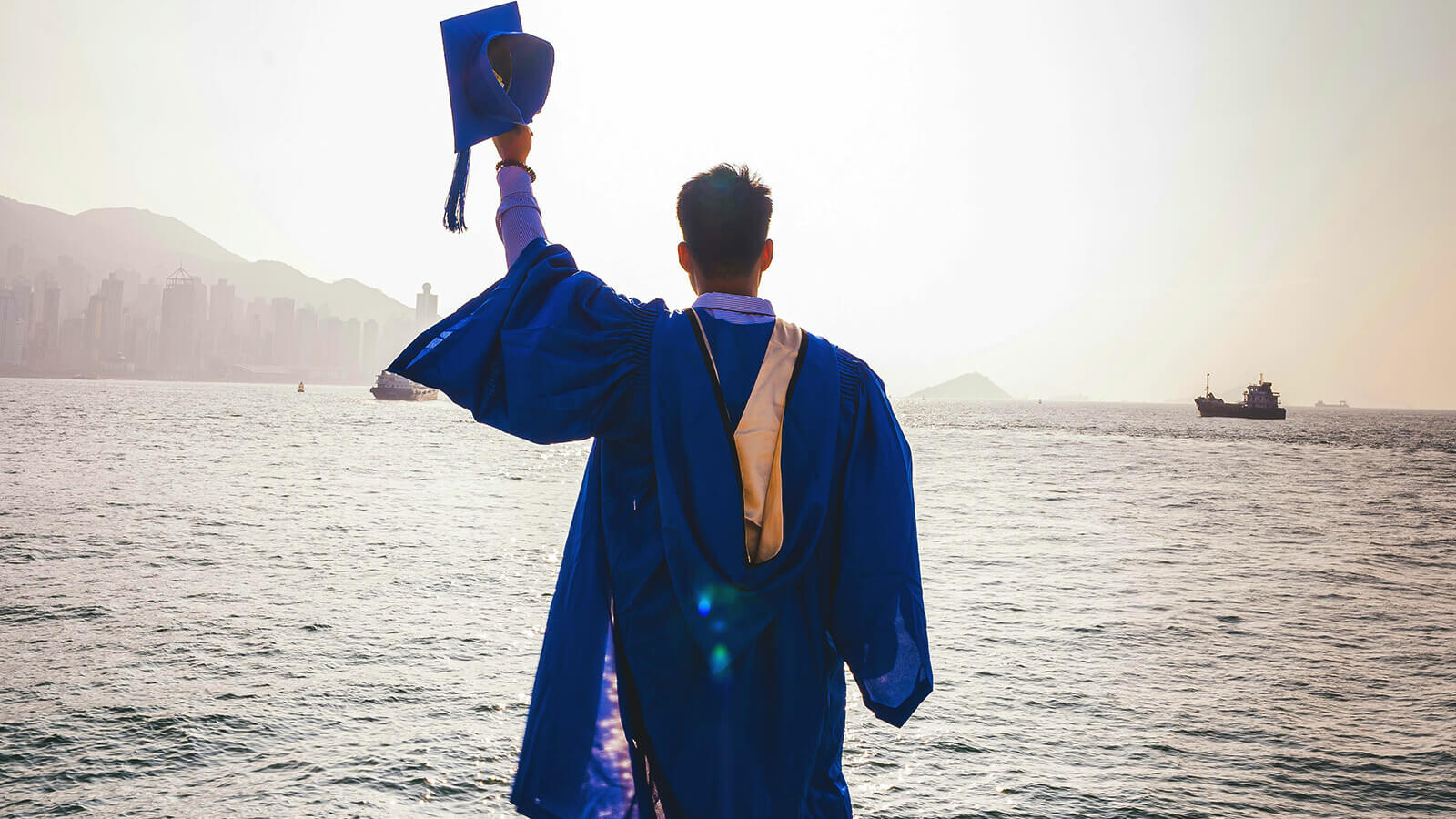 a college graduate in a gap and gown celebrates looking over the ocean