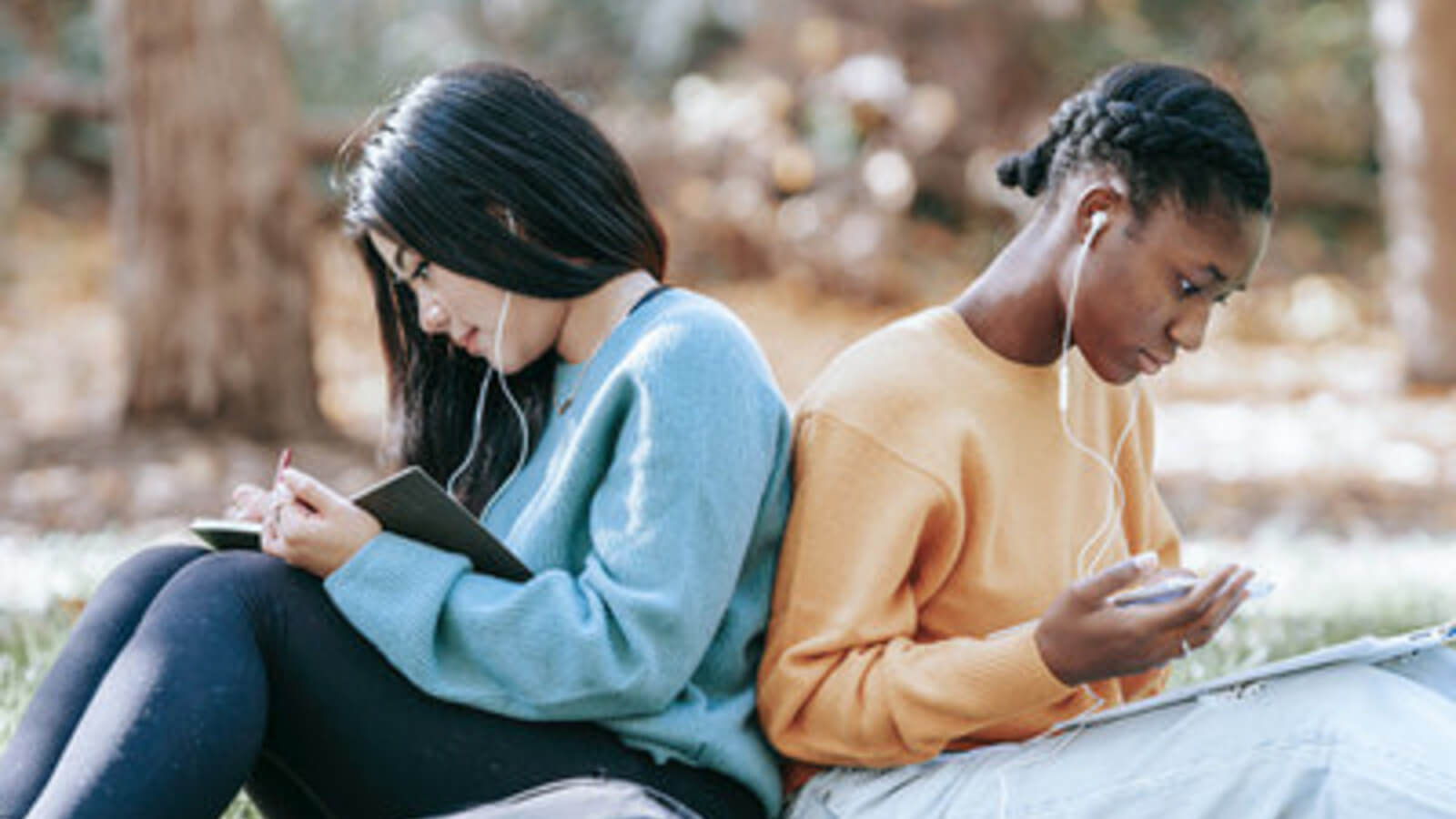 two teen girls sit back to back doing school work