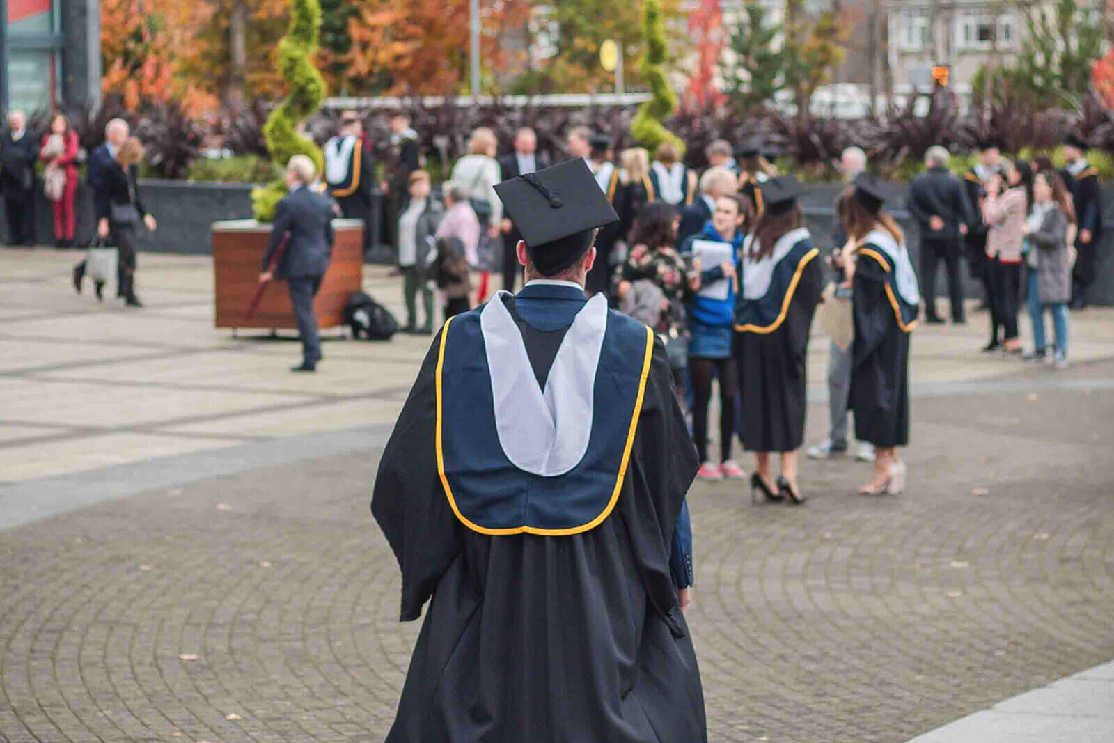 a student pictured from behind in a cap and gown walks at graduation