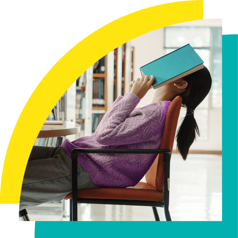 a young woman sitting back in chair with a book covering face