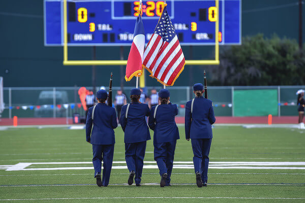 JROTC cadets march with flags on a football field