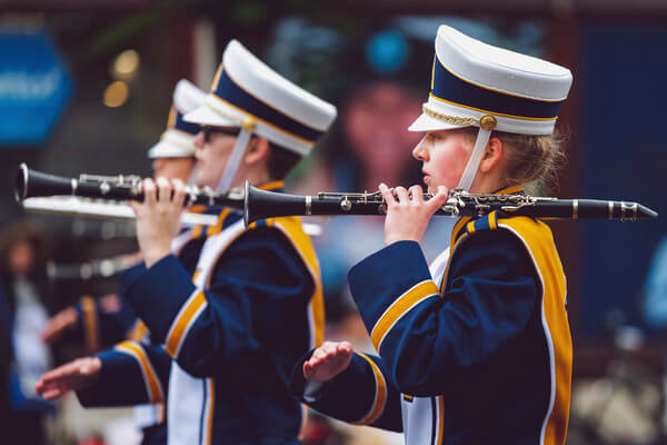 students march in a band wearing blue and gold uniforms and playing instruments