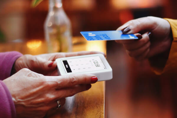 a hand holding a credit card reader as another hand taps to pay