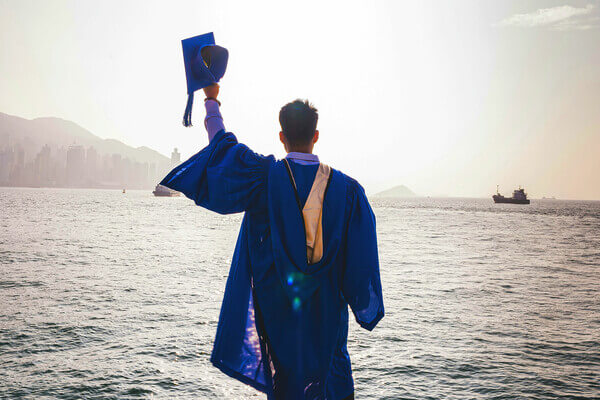 a college graduate in a gap and gown celebrates looking over the ocean