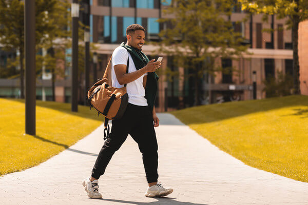 a student walks across campus looking at LinkedIn on a mobile device