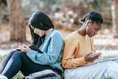 two teen girls sit back to back doing school work